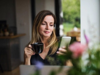 Frau sitzt beim Kaffee mit Smartphone in der Hand